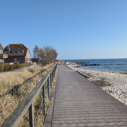 Ein Steg am Strand. Rechts ist das Meer und der Strand von Neustadt in Holstein, links lieht man eine Düne und ein Haus