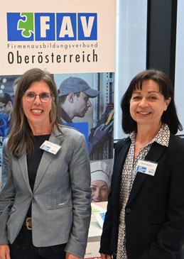 Zwei Teammitglieder des FAV OÖ stehen lächelnd vor einem Rollup