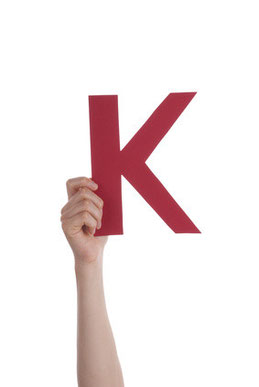 Eine Hand hält einen großen, roten Buchstaben K in die Höhe.