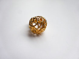 Une bague boule dorée très ajourée est vue de dessus.