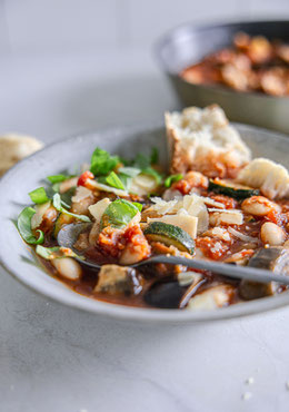 Toskanisches Gemüse-Ragout mit Aubergine, Zucchini, weißen Bohnen und Parmesan, serviert mit frischem Basilikum und knusprigem Baguette