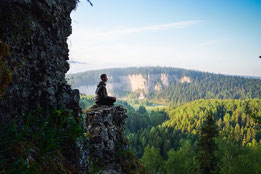 Un méditant assis sur un pic montagneux, la forêt en dessous