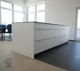 Kücheninsel in weiß mit Keramik-Neolith Arbeitsplatte mit Highboard für Kühl-Gefirrschrank u. Backofen mit brauner, indirekt beleuchteter Nischenrückwand u. Aluminium Griffleiste auf der Front u. flächenbündiger Induktion-Muldenlüfter Siemens