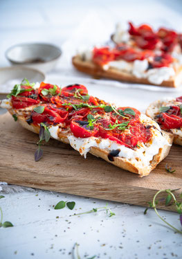 Bruschetta mit Burrata - knusprig, cremig mit geschmorten Tomaten auf einem Holzbrett angerichtet