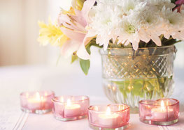 Ein weisser Blumenstrauss in einer Vase und vier rosa Kerzen