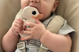 Baby sitzt im Hochstuhl mit einem Beissring aus Naturmaterialien