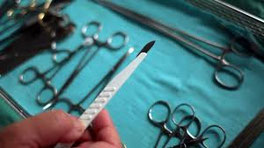 hier befindet sich ein gedeckter OP Tisch und eine Person hält ein Skalpell hoch