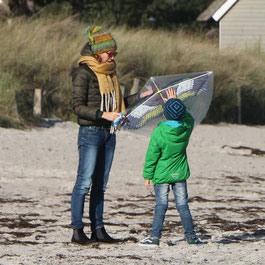 Mutter, die in tragender Beziehung mit Kind einen Drachen am Strand vorbereitet zum Fliegen lassen