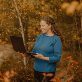 Susanne Kruse steht in herbstlicher Natur und arbeitet am Laptop – Symbol für bewusste, klare und menschlich verbundene Zusammenarbeit im Coaching und Business-Kontext.