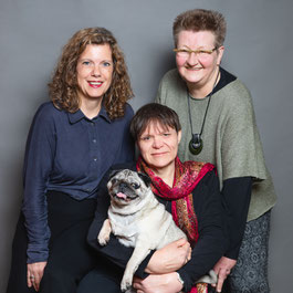 Das Foto zeigt Ilka Haederle, Doris Bewernitz, eine Mopshündin und mich. Wir lächeln in die Kamara und sind verdammt schick gemacht.