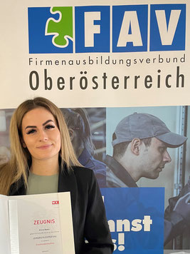 Elvira Ramic posiert vor dem FAV-Roll-Up mit Abschlusszeugnis