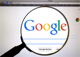 Eine Lupe, die auf einen PC-Bildschirm gerichtet ist, auf dem man groß "Google" erkennt.