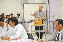 新庁舎の建設位置を無記名投票する委員。手前は他の委員=27日午後、市健康福祉センター