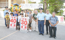 看板設置後に記念写真に収まる関係者ら=15日午後、川平小中学校正門前