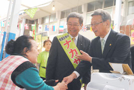 翁長次期知事(右)とともに有権者と握手して回る仲里氏=6日午後、公設市場