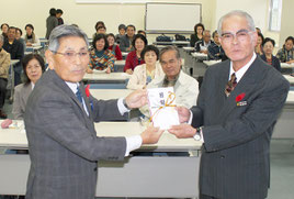 石垣会長(左)から市民生委員・児童委員協議会の東宇里会長に義援金が託された=26日午前、市健康福祉センター