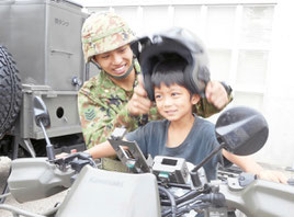 偵察用バイクの乗車体験で、子どもにヘルメットをかぶせる自衛隊員=26日午後、市屋内練習場