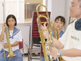 音楽隊からトロンボーンの説明を受け、真剣な表情で見つめる生徒=16日、石垣市総合体育館研修室