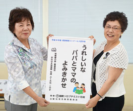 當山会長(左)から石垣教育長にタペストリが贈られた=2日、市教委
