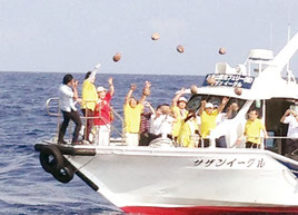 恋路ヶ浜に無事に届くことを願い、一斉にやしの実を投げ入れる参加者たち=19日午前、鳩間島沖(提供写真)