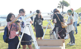 会場に設置された天体望遠鏡を使う来場者たち=15日夕、南ぬ浜町緑地公園