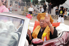 沿道の祝福に手を振って応える竹内さん=3日午前、真栄里公民館