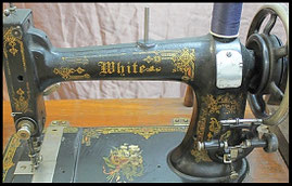 Close-up of an antique White brand sewing machine with ornate gold floral patterns and the name 'White' prominently displayed on its side.