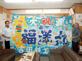 応援メッセージを縫いつけた大漁旗の完成を報告した竹富町=30日午前、町長室