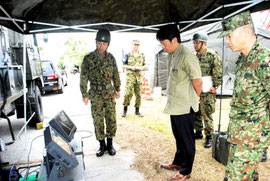 訓練で使用する通信機器について自衛隊員から説明を受ける中山市長=12日午前、バンナ公園