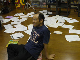 後ろに散らばっている白いモノが台本です。この中から、演出のヤナギサワさんが「どーれーにしよーかな」と選んでいます