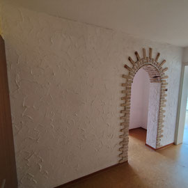 Wand mit sehr groben Putz und Rundbogen.