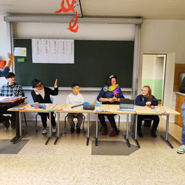 Die Jury sitzt an Tischen vorne im Raum nebeneinander