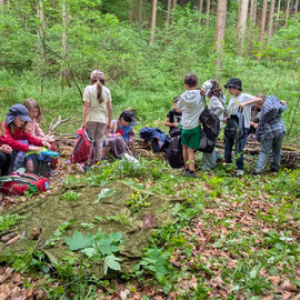 Alle sitzen auf dem selbstgebauten Waldsofa und vespern