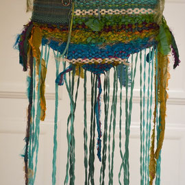 "In Memoriam I - Gebetsfahne zur Erinnerung an Falk" (2012), Freie Weberei, 25 x 54 cm; Material: Wolle, Viskose, Sari-Seidenbänder, Metallgarn, Metallband; kleiner aufgenähter Schal aus Kammgarn mit Gänseaugenmuster, selbst gehämmerter Silberohrring mit 