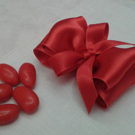 Il nastro di raso, piegato a formare un doppio fiocco contiene i confetti rossi