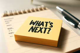 Post-it-Zettel mit Aufschrift "What's Next", der auf einem Schreibblock liegt mit einem Stift daneben.