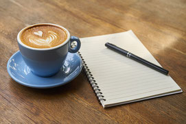 Foto einer blauen Kaffeetasse. Rechts daneben liegen 1 Block und 1 Stift.