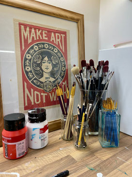 Atelierhoekje van Daphne Schrijver met schilderkwasten, acrylverf en de poster ‘Make Art Not War’ als inspiratiebron voor haar workshops in Breda.