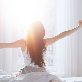 Junge Frau sitzt am Morgen im Bett und streckt sich