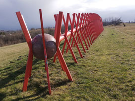 Artwork looking like a centipede consisting of stone balls and red metal rods in a meadow at Pedvale Open Air Sculpture Park in Sabile, Latvia