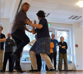 Eine Tai Chi-Gruppe schaut zu, während die Lehrerin etwas zeigt: eine sogenannte Anwendung in den Partnerübungen