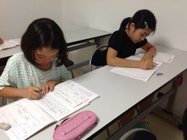 小学生が二人、お手本を見ながら一生懸命、硬筆の練習