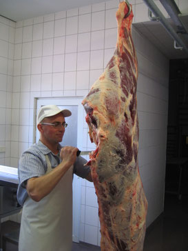 Ein Mann mit Schürze und Messer bearbeitet ein großes Stück rohes Fleisch