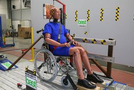 Crash-test dummy sits in a folding wheelchair on a sled. Wheelchair and dummy are secured with Protektor restraint system and head & backrest FutureSafe 