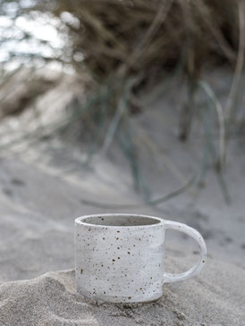 Handgemaakte keramische mok, geïnspireerd door de natuur, in het zand op het strand, omringd door duinen en duingras.