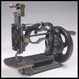 Front view of a vintage White brand hand-cranked sewing machine, featuring elaborate black and gold decorative motifs and a complex gear system.