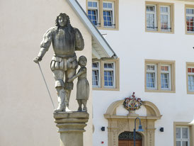 Georg Friedrich von Kaltental und die Waise Adiz - Beton-Plastik von Peter Lenk in Aldingen am Neckar - sowie im Hintergrund das barocke Portal von Schloss Aldingen 