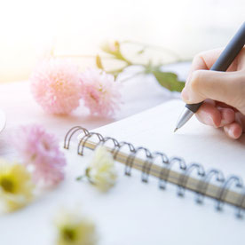 Notizblock, schreibende Hand und Blumen