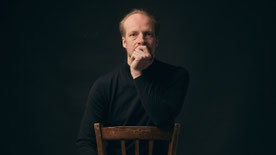 Trompeter Johannes Stange sitzt auf einem Stuhl und schaut nachdenklich in die Kamera