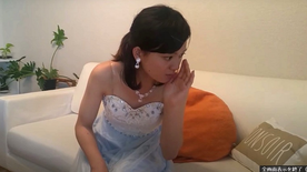 ホステス役を演じる若手女優の佐藤ますみが、ドレス姿でソファに座っている画像
